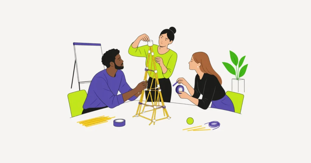 Drei Personen bauen am Tisch einen Turm aus Spaghetti und Klebeband, eine setzt das Marshmallow auf die Spitze