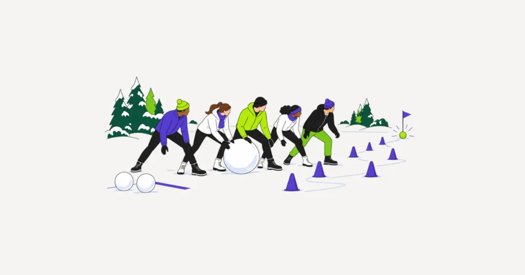 Ein Team in Winterkleidung rollt in einer Reihe eine große Schneekugel entlang einer Hütchenstrecke zum Ziel